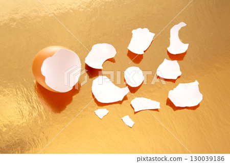 Broken eggs with scattered shells on a shiny golden background Broken eggs with scattered shells on a shiny golden background 130039186