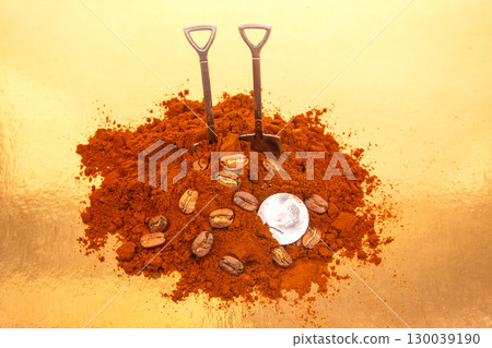 Two shovels in a mound of ground coffee with scattered beans 130039190