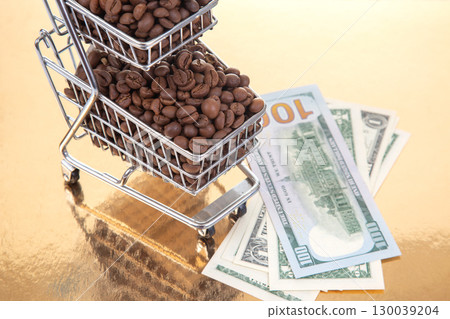 Roasted coffee beans in a small cart with $100 bills on a shiny gold background Roasted coffee beans in a small cart with $100 bills on a shiny gold background 130039204