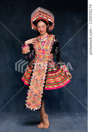 Beautiful Asian woman wearing traditional colorful ethnic costume and silver jewelry, posing in studio portrait. Cultural fashion photography showcasing vibrant embroidery, handmade textile. 130039274