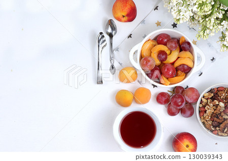 Useful breakfast, food for children, fruit salad with peaches, pears, granola, grapes and flower tea on a bright table. The concept of healthy and natural food. selective focus, top view 130039343
