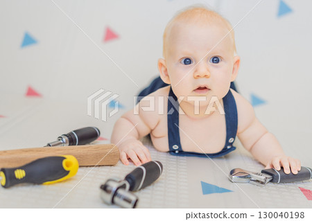 Adorable baby in a mechanic costume surrounded by toy tools. Concept of repair, imaginative play, and introducing kids to the world of fixing and problem-solving through fun 130040198