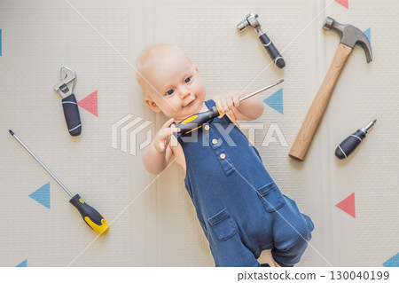 Adorable baby in a mechanic costume surrounded by toy tools. Concept of repair, imaginative play, and introducing kids to the world of fixing and problem-solving through fun 130040199