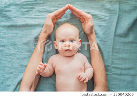 Father hands form a protective roof above baby head. Concept of safety, love, family protection, and emotional security in early childhood 130040206