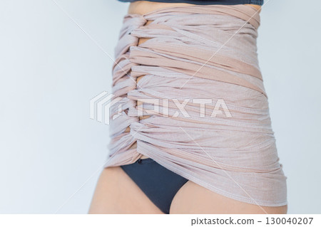 Postpartum woman wraps her belly using Bengkung, a traditional Malaysian belly binding method. Concept of postpartum recovery, cultural practice, and natural healing support 130040207