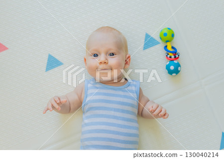 Adorable baby playing with colorful rattles on a soft baby play mat at home. Concept of early development, sensory play, and safe learning environment for infants 130040214