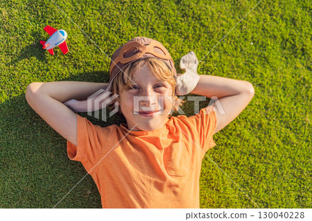 Boy wearing a pilot hat running through the grass with a toy airplane, dreaming of adventures. Childhood, imagination, and freedom concept 130040228