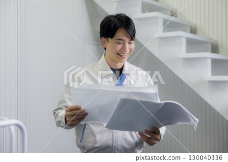 A man in work clothes looking at a blueprint in a warehouse 130040336