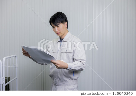 一名身穿工作服的男子正在查看倉庫裡的藍圖 130040340