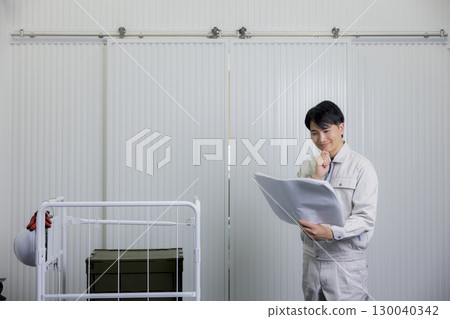 A man in work clothes looking at a blueprint in a warehouse 130040342