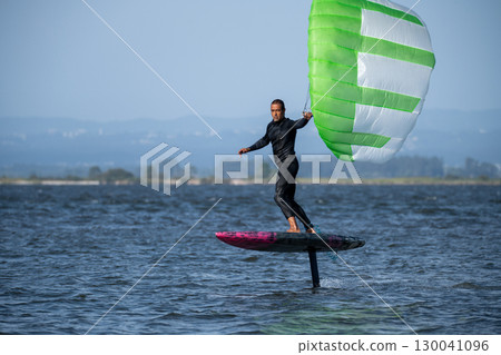 A middle-aged man in a wetsuit on a hydrofoil board glides on the water's surface 130041096