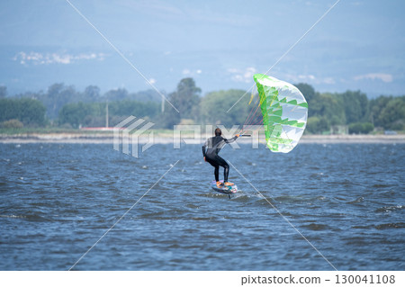 A middle-aged man in a wetsuit glides on a hydrofoil board with a green and white kite 130041108