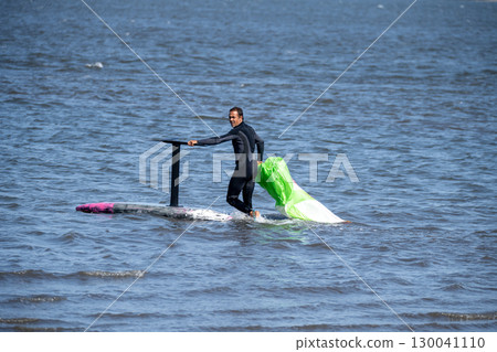 A middle-aged man in a wetsuit on a hydrofoil board prepares to glide 130041110