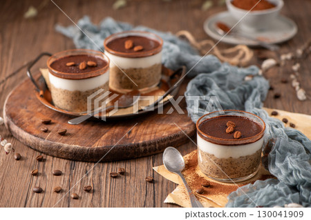 Tiramisu chia puddings elegantly served in glass cups, topped with cocoa powder and coffee beans 130041909