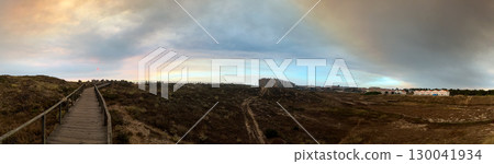 A wide coastal view with a boardwalk leading through sandy terrain A wide coastal view with a boardwalk leading through sandy terrain 130041934