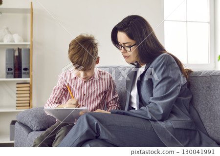 Children's psychologist, therapist or school counselor looking at something little boy is drawing 130041991