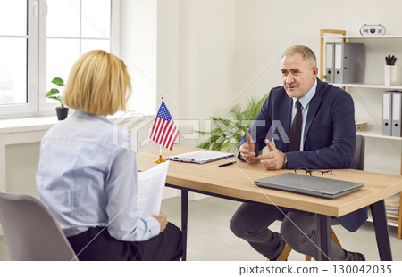 Woman sitting back in office of US public services or embassy and having visa interview. Woman sitting back in office of US public services or embassy and having visa interview. 130042035
