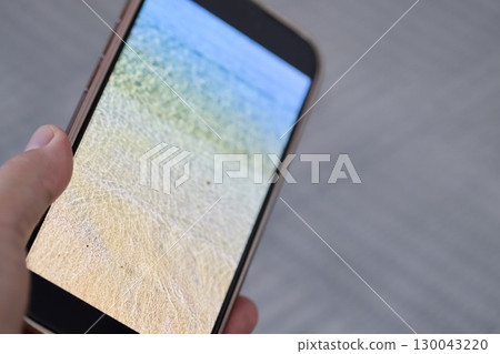 手裡拿著一部帶有海景壁紙的智慧型手機 130043220