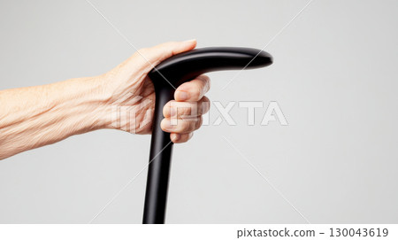 elderly hand grips sleek, modern walking cane against neutral background, showcasing blend of tradition and innovation 130043619