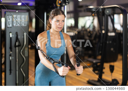 Sportive young girl training on cable tower machine in gym Sportive young girl training on cable tower machine in gym 130044980