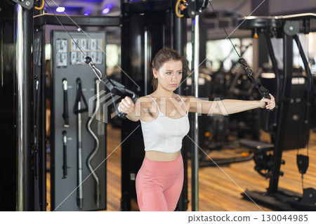 Sportive young girl training on cable tower machine in gym Sportive young girl training on cable tower machine in gym 130044985