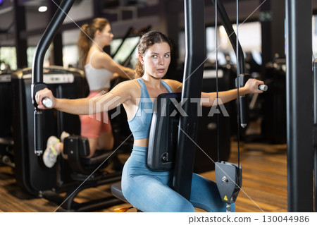 Sportive young girl training on chest fly machine in gym 130044986