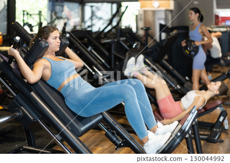 Sportive young girl training on leg press machine in gym Sportive young girl training on leg press machine in gym 130044992