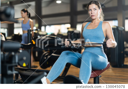 Sportive young girl training on cable row machine in gym Sportive young girl training on cable row machine in gym 130045078