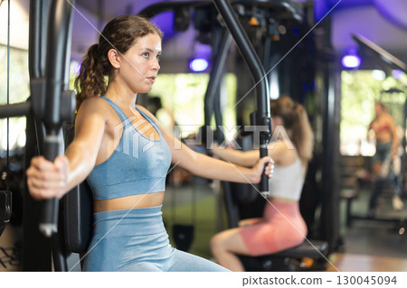 Sportive young girl training on chest fly machine in gym Sportive young girl training on chest fly machine in gym 130045094