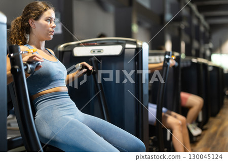 Sportive young girl training on chest press machine in gym 130045124