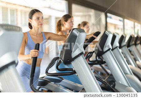 Positive young girl training on elliptical machine in gym 130045135