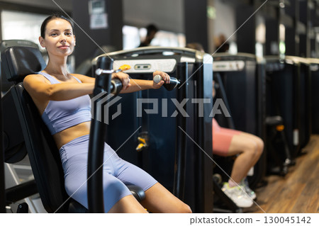 Sportive young girl training on chest press machine in gym 130045142