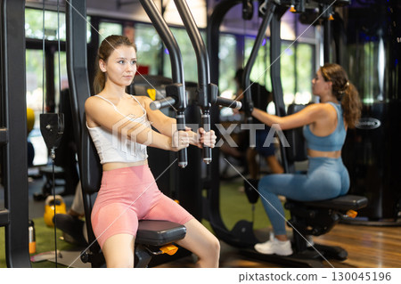 Sportive young girl training on chest fly machine in gym 130045196
