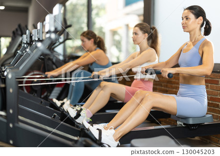 Sportive young girls training on cable row machine in gym 130045203