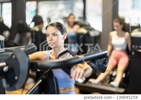 Sportive young girl training on chest press machine in gym Sportive young girl training on chest press machine in gym 130045259