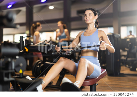 Sportive young girl training on cable row machine in gym Sportive young girl training on cable row machine in gym 130045274