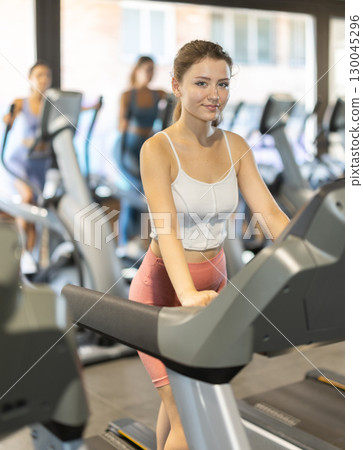 Positive young girl training on treadmill in gym 130045296