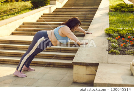 Overweight woman in sportswear doing fitness exercises on stone staircase in city park 130045514