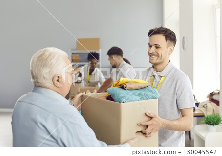 Smiling male volunteer giving senior man box of clothes, providing humanitarian help, social support 130045542