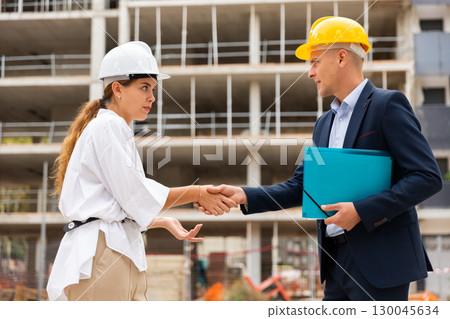 Man and woman in hardhats shaking hands in construction site 130045634