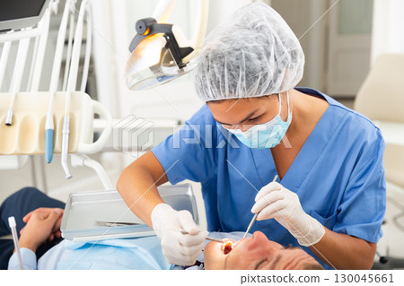 Dentist inspects male patient teeth 130045661