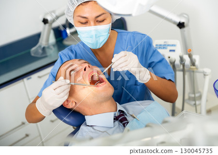 Dentist inspects male patient teeth Dentist inspects male patient teeth 130045735