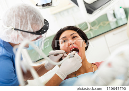 Qualified man dentist in a protective mask treats a woman patient 130045790