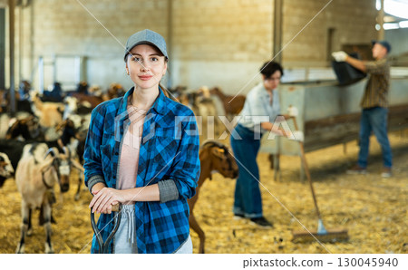 Portrait of young European female farmer in plaid shirt standing with tool while working on goat farm 130045940