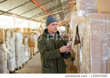 Store warehouse employee scans barcode on boxes using phone 130045990