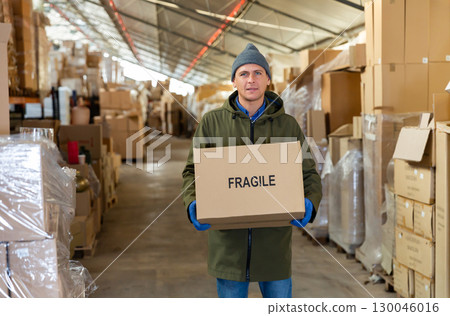 Warehouse worker carrying boxes on racks in in warehouse 130046016