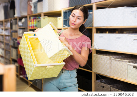 Asian woman chooses wicker fabric box at goods store Asian woman chooses wicker fabric box at goods store 130046108