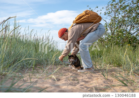 Annoyed guarded cat observes warily while man adjust leash for shoreline walk. Suspicious pet stroll 130046188