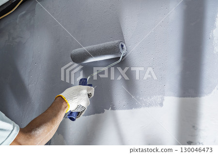 Construction worker in gloves using a paint roller to apply paint to a wall during home renovation. Home renovation project Construction worker in gloves using a paint roller to apply paint to a wall during home renovation. Home renovation project 130046473