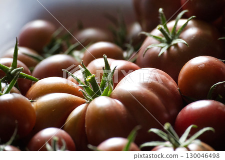 A vibrant image capturing a pile of fresh, ripe, dark tomatoes with green stems. 130046498